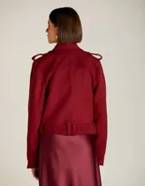 Chaqueta estilo biker de lana color bordó, con solapas amplias, cierre frontal cruzado y cremalleras metálicas doradas. Presenta hombros estructurados, cinturón ajustable en la cintura y forro interno.
