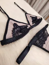 Conjunto de lencería compuesto por un corpiño triangular y una tanga regulable. Está confeccionado en microtul color tostado con detalles de encaje negro en los bordes y en las copas. El corpiño cuenta con breteles finos y la tanga presenta elásticos laterales ajustables.