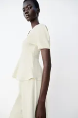 Top peplum confeccionado en hilatura de algodón de color bordó, con escote en V pronunciado, mangas cortas abullonadas y bajo con vuelo.