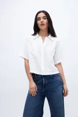 Blusa blanca de corte recto y estilo casual, con cuello camisero, escote en V, cierre frontal con botones y dos bolsillos aplicados en el pecho. Presenta mangas cortas y un acabado texturizado.