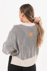 Buzo tejido de punto bicolor en tonos crudo y gris, con silueta relajada, mangas amplias con jaretas regulables en los puños y cuello redondo.