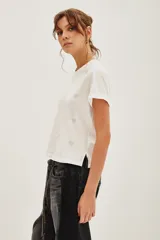Remera blanca de algodón con cuello redondo y mangas cortas con dobladillo. Presenta un estampado sutil de pequeños corazones brillantes distribuidos por toda la prenda.