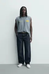 Musculosa de corte relajado con efecto lavado, cuello redondo y sisas amplias. Presenta estampados gráficos en color amarillo en el frente y acabados irregulares que le otorgan una apariencia única.