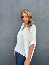 Camisa blanca de corte holgado y asimétrico, con cuello camisero y cierre frontal de botones.