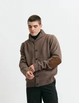 Cardigan de punto color marrón con cuello esmoquin, cierre frontal con botones y presilla superior. Presenta mangas largas con coderas en contraste y bolsillos frontales de ribete.