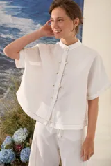 Blusa de lino color blanco, con silueta amplia, cuello mao y cartera frontal con botones dorados.