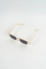 Lentes de sol con armazón grueso y rectangular de color beige claro, con lentes oscuros.
