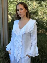 Camisa de lino azul marino con volados en cascada a lo largo del frente y en los puños de las mangas largas. Presenta un escote en V con un botón de nácar visible.