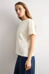 Remera azul marino de manga corta, corte recto y cuello redondo, con detalle de aplicación bordada de flores de crochet en el lateral inferior.