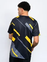 Remera de entrenamiento Fynar del Club Atlético Peñarol, color negro con estampado geométrico en amarillo y gris. Presenta cuello redondo, mangas cortas y el escudo del club en el pecho.
