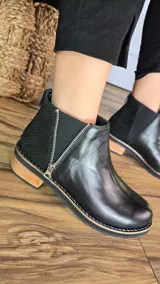 Botinetas de cuero napa color tostado, con taco bajo de madera de 3 cm, elástico lateral y panel trasero con textura de símil piel de serpiente. Cuentan con un cierre lateral decorativo y funcional.
