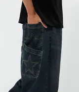 Pantalón jean de corte super baggy, color azul oscuro con efecto lavado, confeccionado en algodón. Presenta un diseño holgado de tiro alto, con bolsillos laterales y traseros, destacando un detalle de estrella aplicado en uno de los bolsillos posteriores.