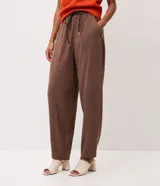 Pantalón carrot color marrón de modelado suelto en la cadera con barra afinada, cintura elástica con amarre ajustable y bolsillos.