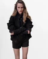 Chaqueta marrón oscuro de piel caprino, con cierre frontal de botones, bolsillos con solapa en el pecho y mangas largas.