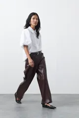 Pantalón de cuero sintético en color marrón oscuro, con corte flare, tiro medio y costuras frontales verticales que estilizan la silueta.