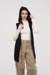 Chaleco largo sin mangas de tejido de punto color negro, con capucha y lazo ajustable en la cintura. Presenta bolsillos frontales y diseño abierto.