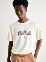 Remera beige de manga corta con estampa frontal con la palabra 'Tropican' en letras negras y detalles en color bordó.