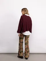 Sweater de punto oversize en color bordó con destellos de lurex. Presenta un diseño acanalado vertical, cuello redondo y mangas largas con terminaciones acampanadas y bordes ondulados.