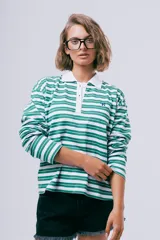 Camiseta estilo polo de manga larga con diseño de rayas horizontales verdes y blancas, cuello blanco y cierre frontal con botones. Presenta un pequeño bordado azul en el pecho.