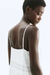 Vestido corto blanco con breteles finos ajustables, escote cuadrado y cuerpo con paneles verticales de encaje calado.