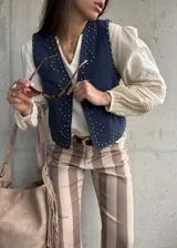 Chaleco de jean oscuro con tachas doradas aplicadas en la parte frontal y escote en V.