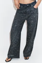 Jeans de tiro medio con corte baggy y cinco bolsillos. Presenta un diseño de estampado floral realizado con aplicaciones de strass a contraste sobre el tejido denim.