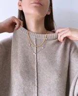 Buzo de tejido de punto color visón, con diseño holgado, cuello redondo, mangas largas con puños acanalados y costura central vertical visible. Presenta un ruedo asimétrico con aberturas laterales.