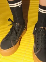 Championes de lona negra con plataforma y puntera de goma marrón, cordones negros y costuras en contraste.