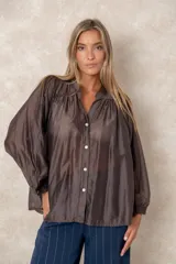 Camisa de organza blanca con cuello mao, diseño de manga larga tipo murciélago y cierre frontal con botones. Presenta un corte holgado y fluido.