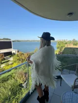 Ruana de lana merino color crudo, con diseño tejido de punto grueso y terminaciones con flecos largos en todo el borde.