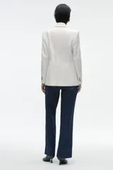 Blazer de corte entallado con cuello y solapa, manga larga y hombros marcados. Presenta un cierre frontal cruzado con botones dorados y bolsillos delanteros con solapa.