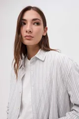 Camisa de corte oversize con diseño de rayas verticales finas en tonos claros. Presenta cuello clásico, cierre frontal con botones y mangas largas con puños abotonados.