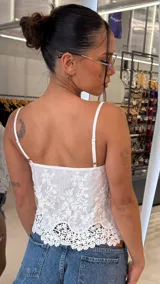 Top blanco de tirantes finos y escote en V, con delicados bordados florales y detalle de lazo frontal. El ruedo presenta un diseño de encaje festoneado.