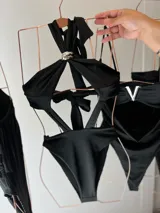 Body negro con escote halter y aro metálico plateado que crea un efecto drapeado en el busto. Presenta tiras cruzadas en la espalda y está confeccionado en tela elastizada.