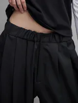 Pantalón sastrero negro de satén, con cintura elástica, tiro bajo, pinzas delanteras, bolsillos laterales y bolsillo ojal trasero.