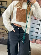 Sweater tejido de punto en color crema, con corte holgado y manga larga. Presenta un aplique rectangular central de cuero genuino con un mapa grabado.