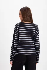 Remera de manga larga con diseño oversize, confeccionada en tejido de punto grueso a rayas horizontales en tonos marrón y blanco. Presenta cuello redondo y un pequeño bordado distintivo en el pecho.