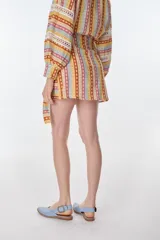 Minifalda estampada con motivos geométricos en tonos amarillo, naranja, celeste y rosa. Tiene corte evasé y lazo para ajustar en la cintura.