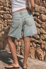 Bermuda de tiro medio confeccionada en denim de color negro gastado, con diseño de cinco bolsillos, trabillas para cinturón y cierre frontal con cremallera y botón metálico.