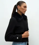 Saco corto de polivelour negro con cuello de piel sintética, cierre frontal oculto, bolsillos cargo delanteros con solapa y detalles de botones en los puños.