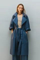 Trench oversize y largo de color azul, con doble cruce al frente, solapas amplias, bolsillos laterales y lazo para anudar en la cintura. Confeccionado en gabardina de algodón.