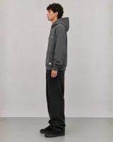 Canguro con capucha y cordones ajustables, de color gris oscuro con efecto lavado. Presenta un bolsillo frontal tipo canguro y estampado gráfico pequeño en el pecho con el logo de la marca.