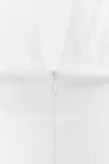 Vestido mini de color blanco con cuello halter, escote en pico y falda con vuelo tipo capa. Presenta cierre con cremallera oculta en la espalda y lazada en el cuello.