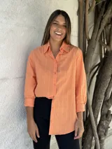 Camisa color salmón con cuello clásico, cierre frontal con botones y mangas largas con puños abotonados.