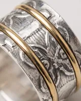 Anillo ancho de plata con detalles grabados de mariposa y dos finas líneas superpuestas en tono dorado.