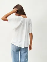 Blusa blanca de manga corta con textura arrugada, escote redondo con abertura en V y lazos ajustables. Presenta detalles de puntilla calada en los hombros.
