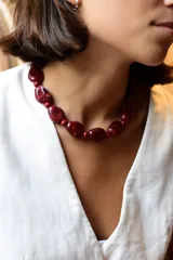 Collar de cuentas de resina en tono bordó con vetas blancas, intercaladas con pequeñas esferas del mismo material. Cuenta con cadena de acero quirúrgico para regular el largo.