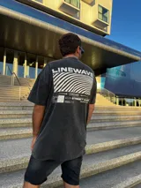 Remera negra con efecto gastado, corte amplio y estampado en la espalda con la palabra "Linewave" y un diseño de ondas blancas.