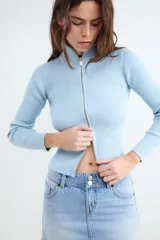 Sweater de punto celeste con diseño acanalado, cuello alto y cierre frontal con doble cremallera metálica, de manga larga y calce al cuerpo.