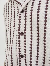 Camisa resort de manga corta color beige, con patrón geométrico de rayas verticales en tonos bordó, cuello camisero, cierre frontal de botones y calce relajado.